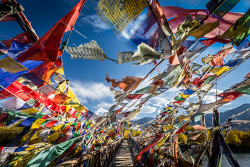 Colourful Buddhist prayer flags on a bridge above Indus river in the Himalayan mountain, Leh,...