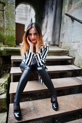 Obraz na płótnie Canvas Fashionable woman look with black and white striped suit jacket, leather pants, posing at old street on iron stairs. Concept of fashion girl.