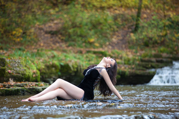 Portrait of a brunette in a black dress near a mountain river. The model is posing at the waterfall.