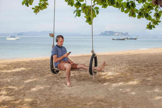 The man is sitting on a swing and reading an e-book. Lifestyle concept. Thailand, Krabi. February 2017.