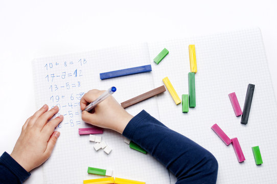 Open exercise book with colored plastic math learning tools number rods on white background. Close-up of children's hands. solving mathematics examples. Educational and school concept.