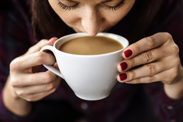 White young woman holding a cup of coffee in her hands and drinking it while coffee break.