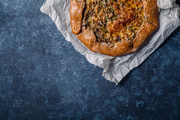 French styled leek and onion galette with sage and gruyere cheese made with wholegrain flour. Textured blue background. Rustic concept with copy space
