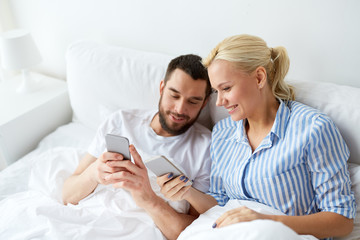 happy couple with smartphones in bed at home