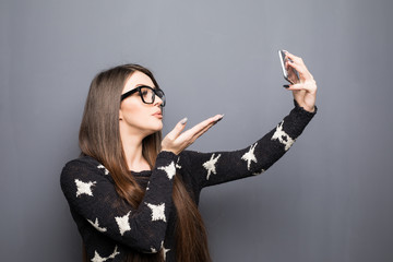 Young pretty girl making a selfie and sending a kiss on gray background