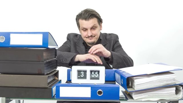 A young worker is feeling sleepy five minutes before the end of a work day. He puts his head on a desk. His workdesk is full of folders and documents.