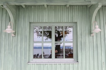 White vintage window in a white-green painted wooden house wall with reflexions of surrounding items