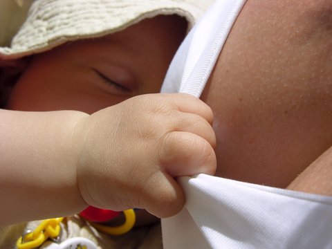 Vier Monate alter Junge (Baby) schläft im Tragetuch und hält sich an Mamas Bluse fest