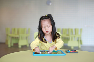 Little asian child girl playing chalk on blackboard in kids room.