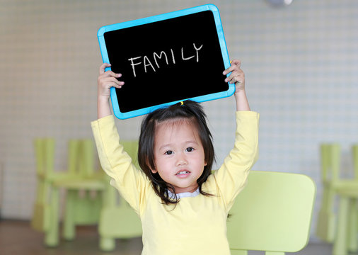 Cute little child girl holding blackboard showing text " FAMILY " in kids room. Education concept.