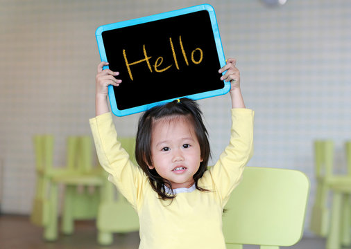 Cute little child girl holding blackboard showing text " Hello " in kids room. Education concept.