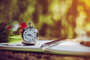 pen, packet watch and rose  on the desk, open a blank white notebook on table