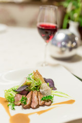 Filet of meat with field salad on plate and red wine