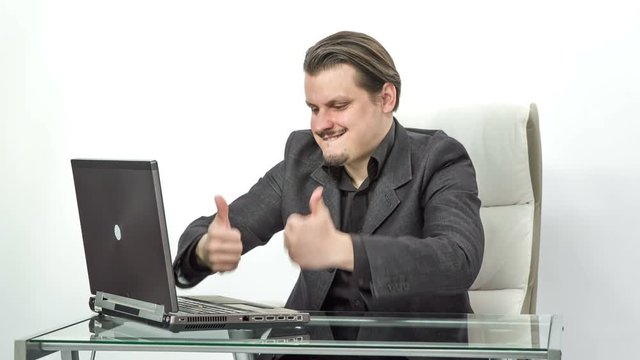 A man behind his computer is excited about something and he shows thumbs. He is very happy.