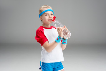 side view of girl in sportswear drinking water isolated on grey