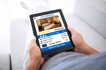man on sofa holding tablet with app hotel booking screen