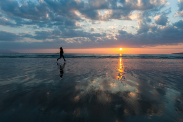 Silhouette of woman in the distance running on the beach at sunset 