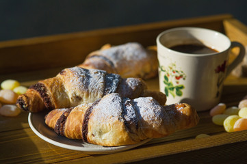 Breakfast still life, fresh croissants and cup of morning coffee on a wooden tray