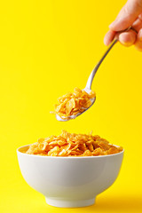 Corn flakes bowl on a yellow background. Hand holding a corn flakes spoon. Eating breakfast.