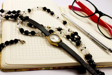 A close-up of a coffee table with a set for a business lady: a notepad, pen, glasses for protection from the computer, beads and watches
