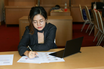 Fototapeta na wymiar working woman in black dress who wear glasses look at charts paper on wooden desk
