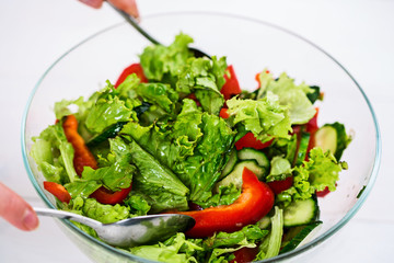 Young woman dressing vegetable salad with olive oil on a white background
