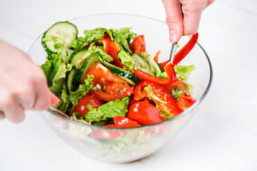 Young woman dressing vegetable salad with olive oil on a white background