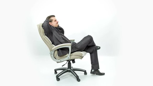 A young man is relaxing back in his chair and is putting hands behind his neck. He looks calm and happy.