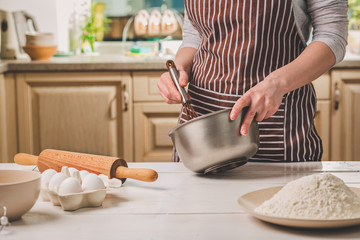 Young woman holding bowl with dough and whisk, closeup