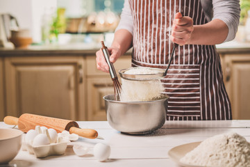 Young woman holding bowl with dough and whisk, closeup