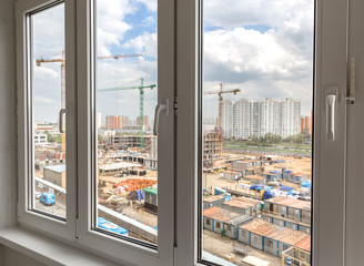 Closed plastic windows. Blurred view of construction site and cloudy sky outside the windows