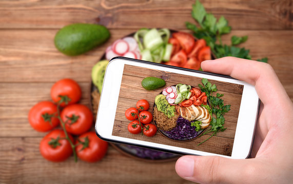 Hands taking photo salad bowl with quinoa, chicken, avocado and vegetables with smartphone.