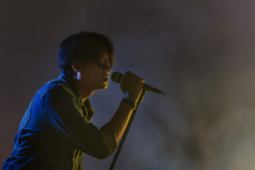 A man singing into a microphone under spotlight with smoke on a stage