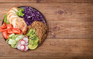 Healthy salad bowl with quinoa, chicken, avocado and vegetables on wooden background .
