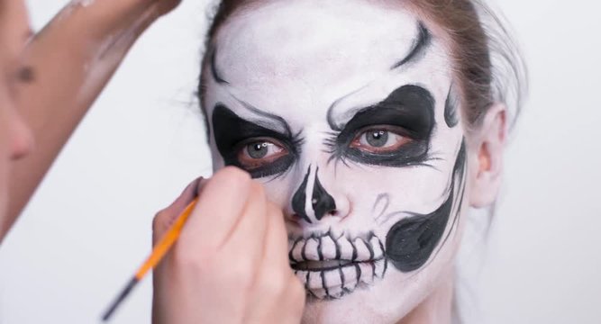 Make-up artist make the girl halloween make up on white background. Halloween face art.