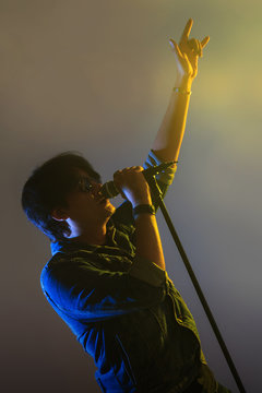 A man singing into a microphone under spotlight with smoke on a stage