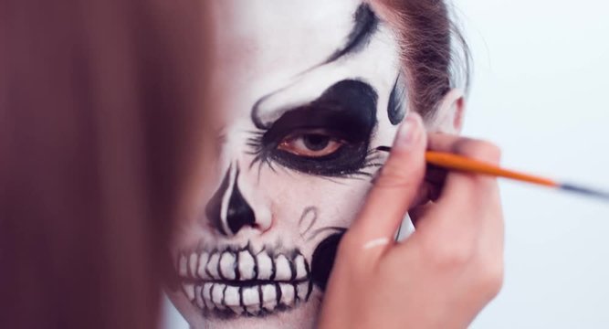 Make-up artist make the girl halloween make up on white background. Halloween face art.