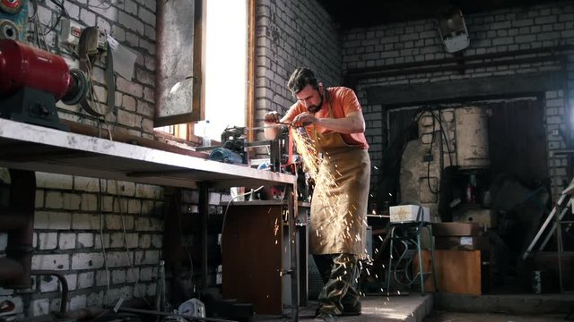 Blacksmith in forge - sharpening iron tools with sparkles - metal workshop