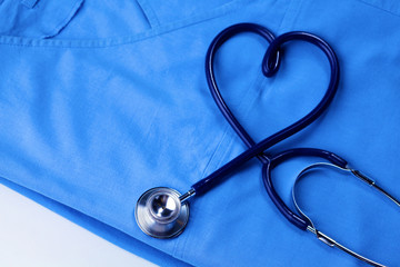 Medical stethoscope twisted in heart shape lying on patient medical history list and blue doctor uniform closeup