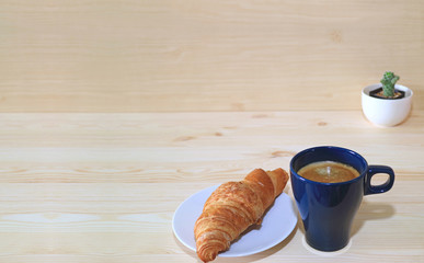 Coffee, butter croissant and a mini cactus plants on the wooden table with free space for text and design
