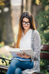 A shot of a college student reading a book on bench in park