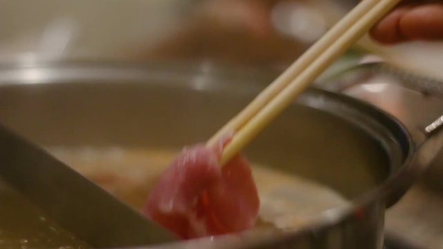 Close up shot hand of woman use chopsticks putting slide pork into the hot pot