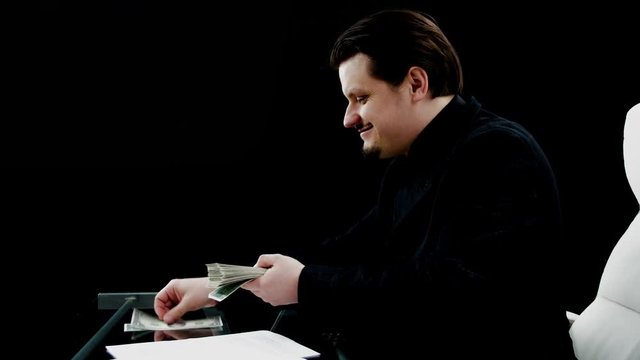 A young businessman takes the money out of his pocket and starts counting it. He has a smile on his face.