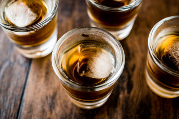 Whiskey Shots with ice on dark wooden surface.