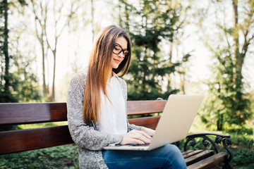 Young girl on a bench with a laptop in park