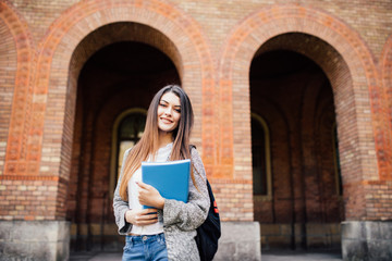 Fototapeta na wymiar smiling teenage girl with folders and bag in university background