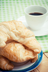 Coffee with fresh croissant breakfast on wooden table.