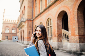 Single student walking and speak mobile phone with a university building in the background
