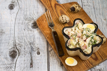Fototapeta na wymiar Salad. Freshly prepared salad in a figured ceramic salad bowl, quail eggs and fork on a cutting board on a gray wooden background. 
