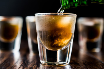 Pouring Whiskey Shots with ice on dark wooden surface.